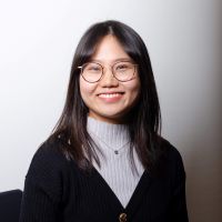Dr Jing Xu, a Chinese woman is sitting smiling directly into the camera. She has shoulder-length dark hair and glasses